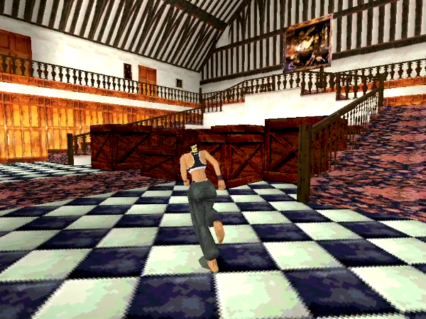 Ein Screenshot aus Tomb Raider. Bildmittig Lara Croft in Sportkleidung. Dahinter Holzkisten auf einem schwarz-weiß gefliesten Boden. Im Hintergrund rechts und links offene Treppen, die zur Galerie hinauf führen. An der Rückwand des Foyers Gemälde und Türen.